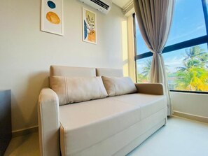 Ein beiges Sofa in einem Raum mit großem Fenster, Klimaanlage und zwei Wandbildern.