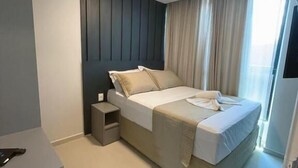 A modern bedroom with a bed, bedside tables, and a window with curtains. - Ocean Porto Flats (Ipojuca)