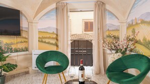 A room with a mural, two green chairs, a table with a bottle and glasses, and a fireplace with a shutter. - Condotta House, a private space in the heart of historical center of Florence (Firenze)