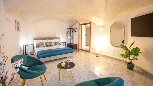 A bedroom with a bed, bedside table, lamp, potted plant, and a chair. - Condotta House, a private space in the heart of historical center of Florence (Firenze)