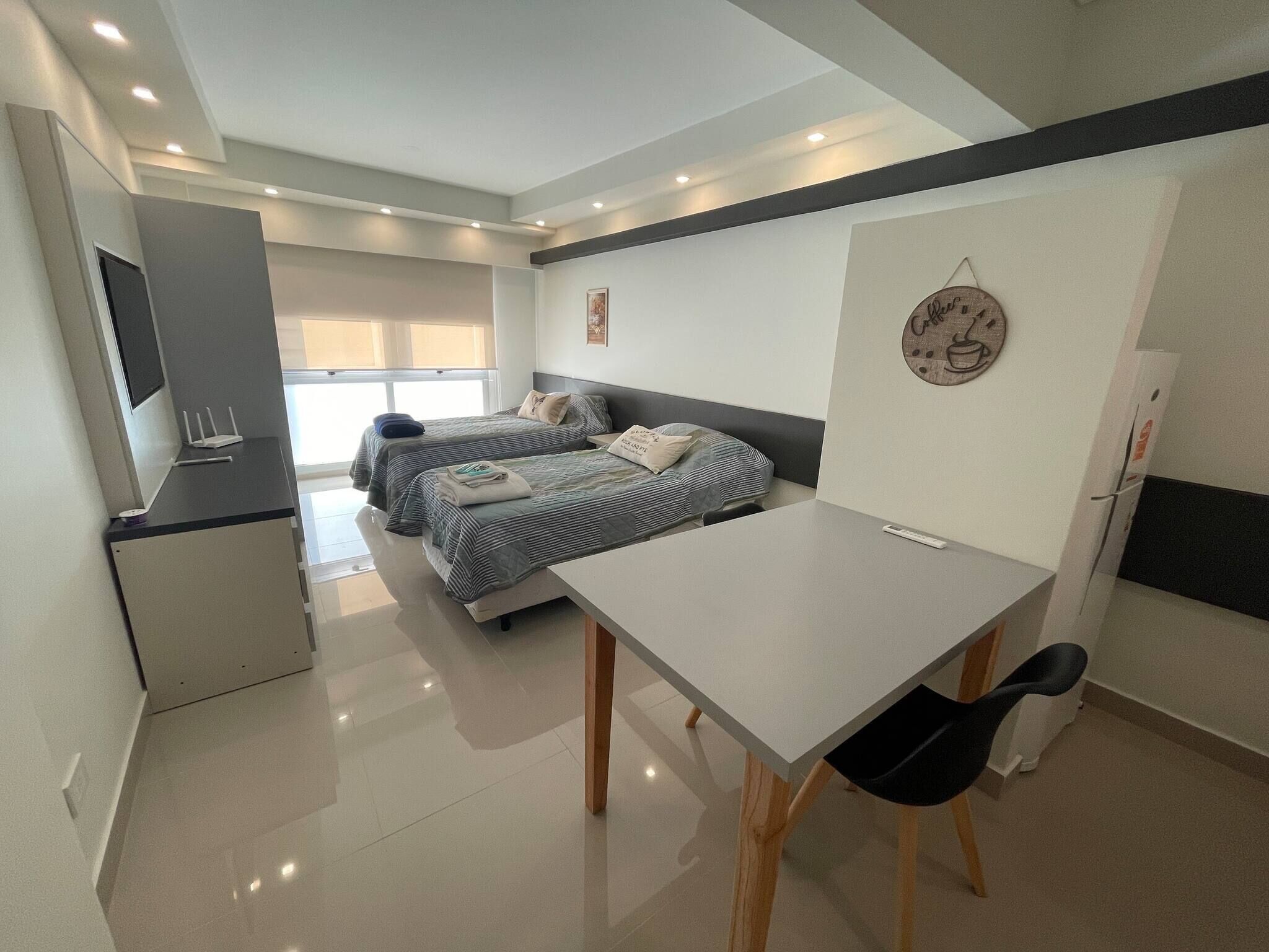 Una habitación moderna, bien iluminada, con dos camas, un escritorio y una silla.