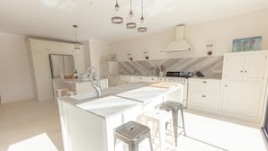 A modern kitchen with white cabinetry, a central island with stools, stainless steel appliances, and pendant lighting.