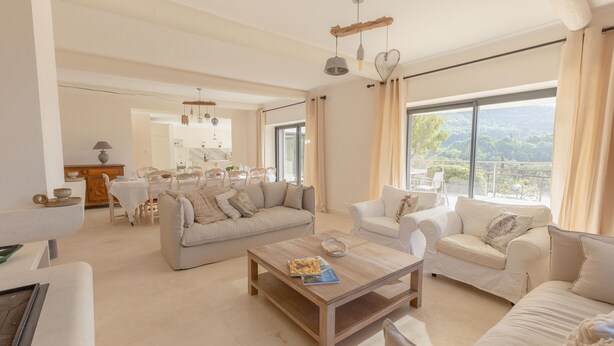 A spacious living room with a wooden coffee table, two white sofas, and a dining area in the background.