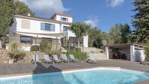 A two-story house with a swimming pool, outdoor seating, and a stone wall.