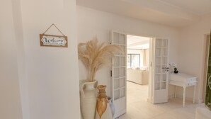 A hallway with a 'Welcome to our home' sign, large vases, and a white door leading to another room.