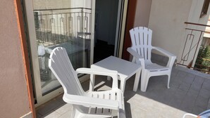 Een balkon met twee witte plastic stoelen, een kleine tafel, een glazen deur en een metalen hekwerk.