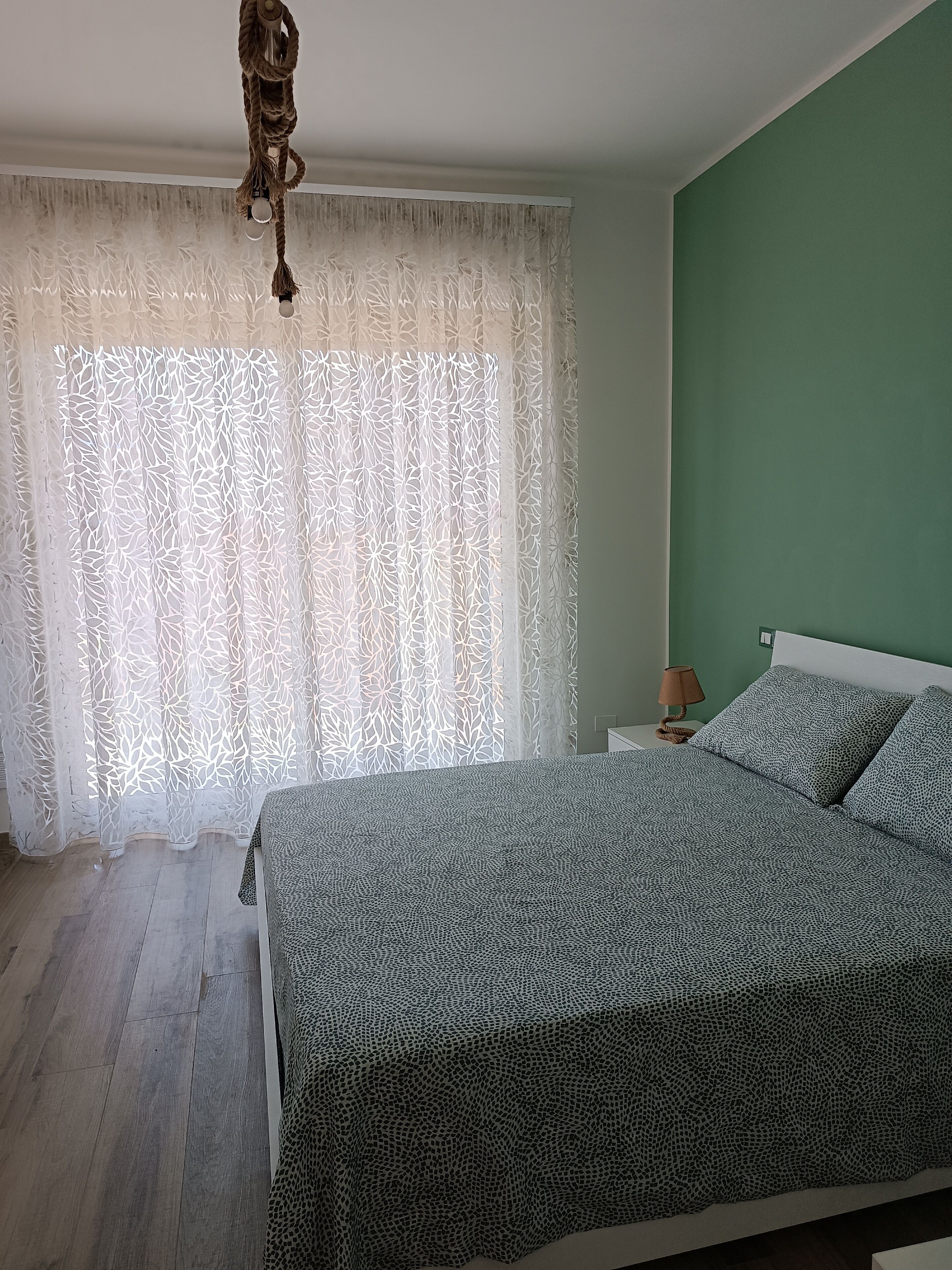 A bedroom with a bed, a nightstand, a lamp, and a decorative rope hanging from the ceiling.