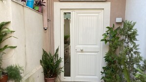 Een smalle binnenplaats met een witte deur, plantenpotten en een betegelde vloer.