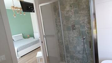 Eine gläserne Dusche mit gefliestem Wandbereich, Holzboden und einem Bett, wobei eine grüne Wand im Hintergrund zu sehen ist.
