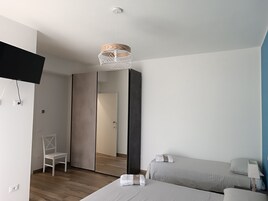 Quarto de hotel moderno com cama, uma cadeira, escrivaninha e televisão.