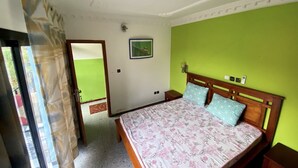 Une chambre à coucher avec un lit, une table de chevet, un mur vert et une porte donnant sur une autre pièce.
