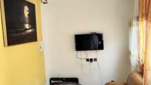 Un salon avec un téléviseur à écran plat fixé au mur, un lustre, un canapé et une table basse.