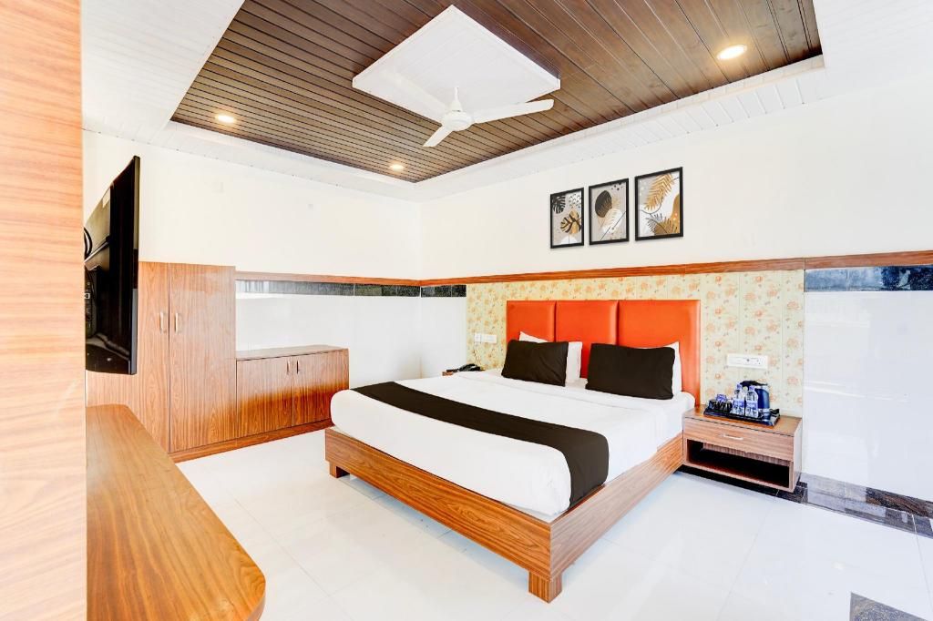 A modern hotel room with a wooden bed, a flat-screen TV, a small bedside table, and a ceiling fan.