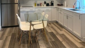 Een moderne keuken met een roestvrijstalen koelkast, een glazen eettafel met witte stoelen en inbouwkeukens.