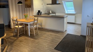 A modern kitchen with a dining area, featuring a wooden table, chairs, a coffee maker, and a window providing natural light. - Urlaub auf dem Bauernhof in der Nähe von Sankt Peter Ording (Tating)