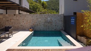 Una piscina con muro de piedra, terraza de madera y zona de estar cubierta.