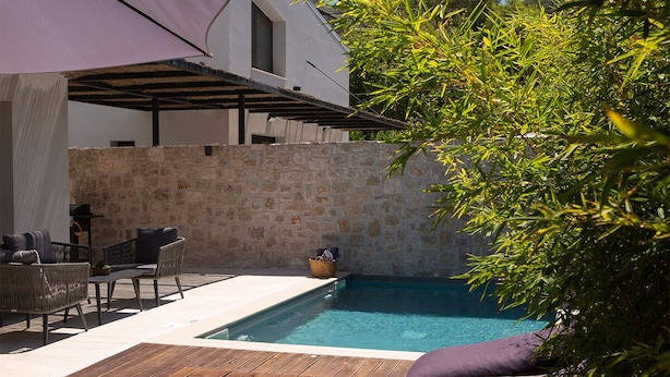 Una piscina con muro de piedra, mobiliario exterior y una pérgola.