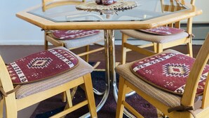 Una mesa redonda de vidrio con un mantel tejido, rodeada de sillas de madera con cojines estampados.