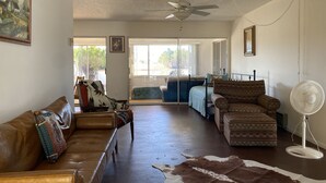 Un salón con un sofá de cuero marrón, un sillón estampado, un tapiz de piel de vaca y un ventilador blanco.