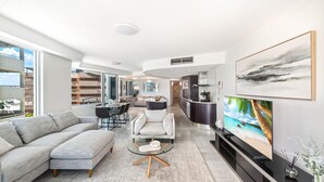 Una sala moderna con sofá, mesa de centro y televisor. Hay un comedor con mesa y sillas, además de una cocina con refrigerador y estufa.