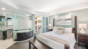 Un dormitorio moderno con una cama grande, lámparas de noche, una ducha con cerramiento de vidrio y vistas al mar a través de un ventanal amplio.