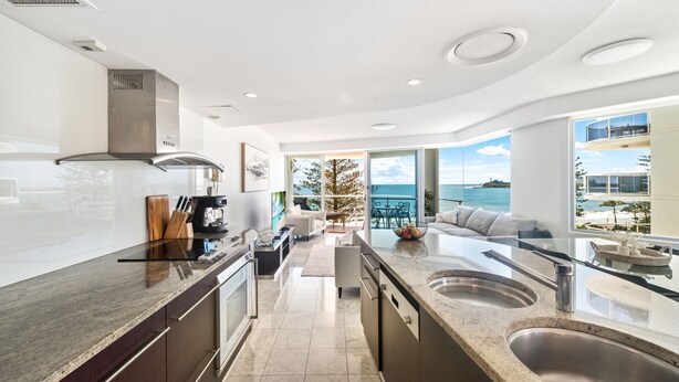 Una cocina moderna con una isla central, una zona de comedor con vistas al mar y un área de estar con sofá y mesa de centro.