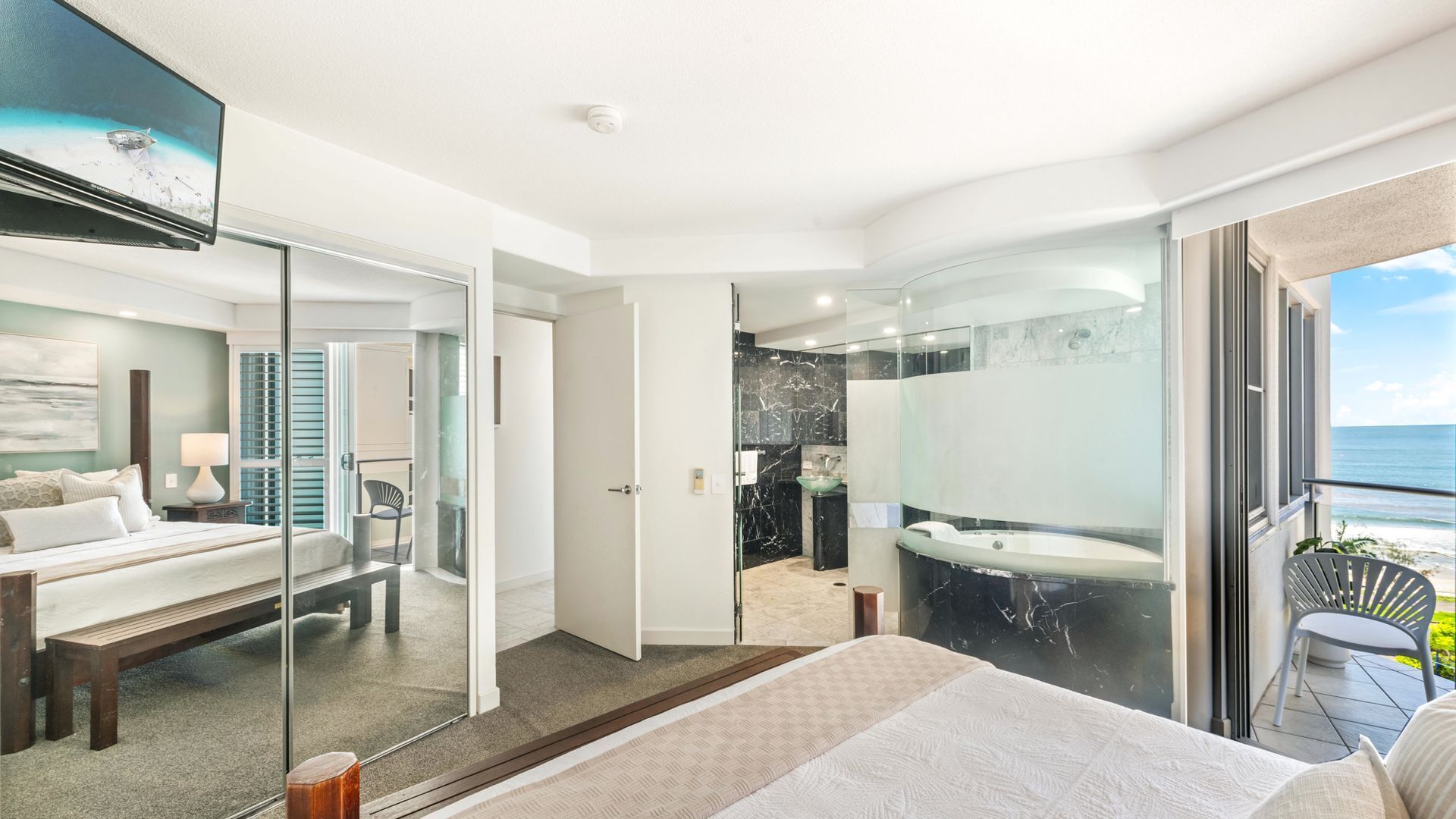 Quarto de hotel moderno com uma cama grande, banheiro com banheira e varanda com vista para o oceano.