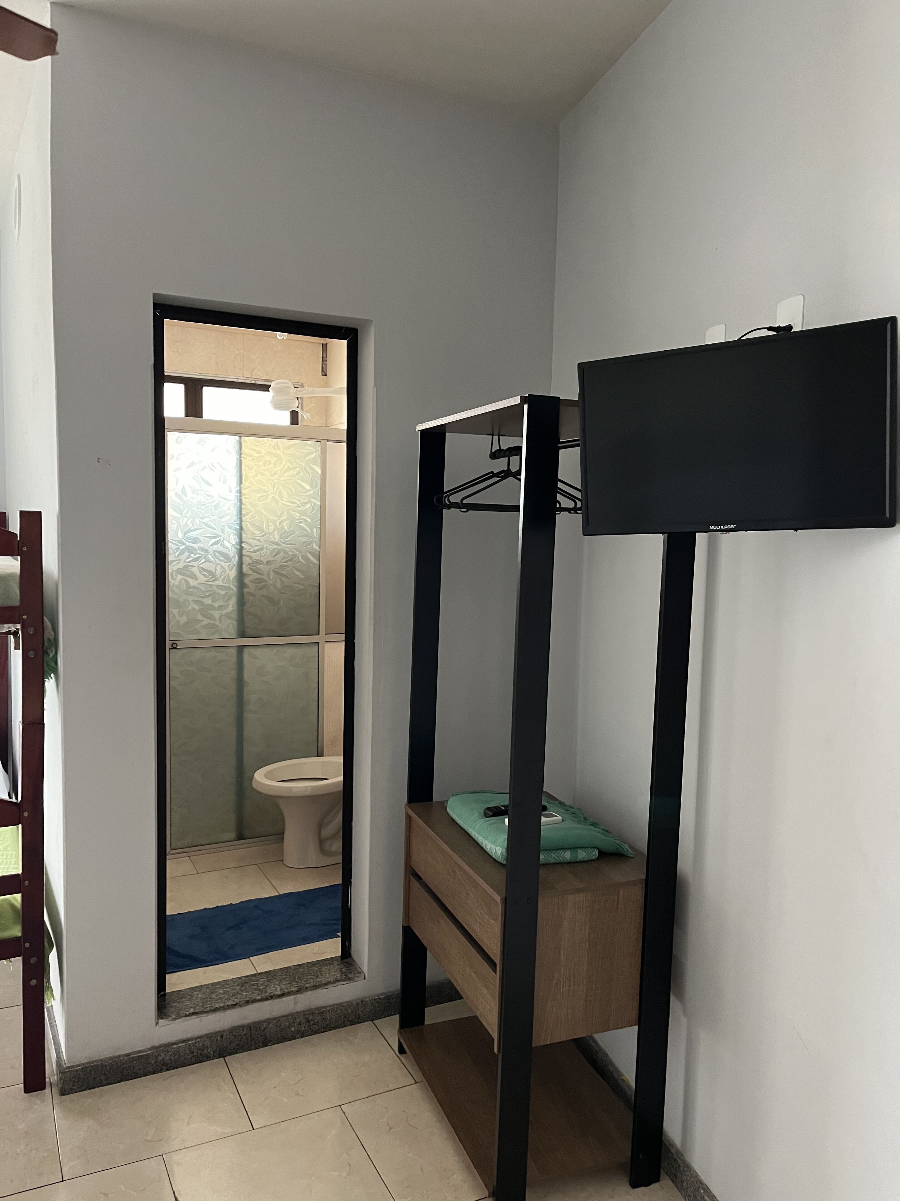 A room with a bunk bed, a small table, and a mirror. There is a door leading to a bathroom with a toilet and a shower.