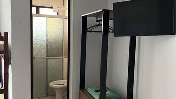 A room with a bunk bed, a small table, and a mirror. There is a door leading to a bathroom with a toilet and a shower.