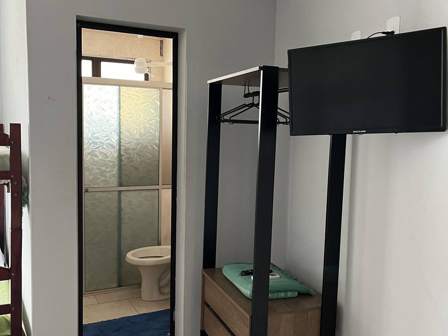 A room with a bunk bed, a small table, and a mirror. There is a door leading to a bathroom with a toilet and a shower.