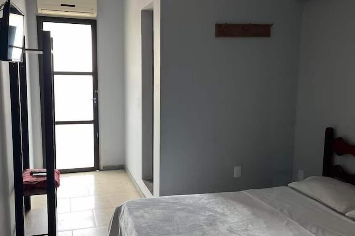 Un dormitorio con una cama, un escritorio y una silla. Hay una ventana y una puerta.