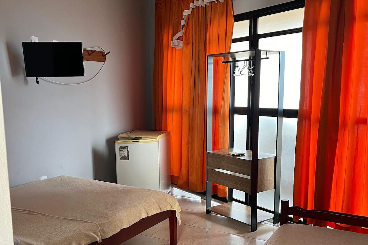 Habitación de hotel con dos camas de madera, un televisor montado en la pared, un refrigerador pequeño y un escritorio con una silla.