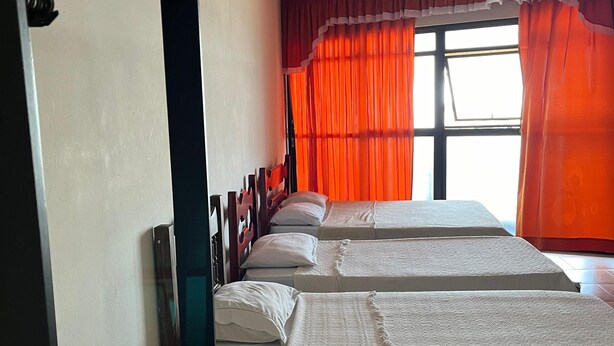 A hotel room with two beds, a ceiling fan, and a window with orange curtains. - Hotel Art Final (Marataizes)