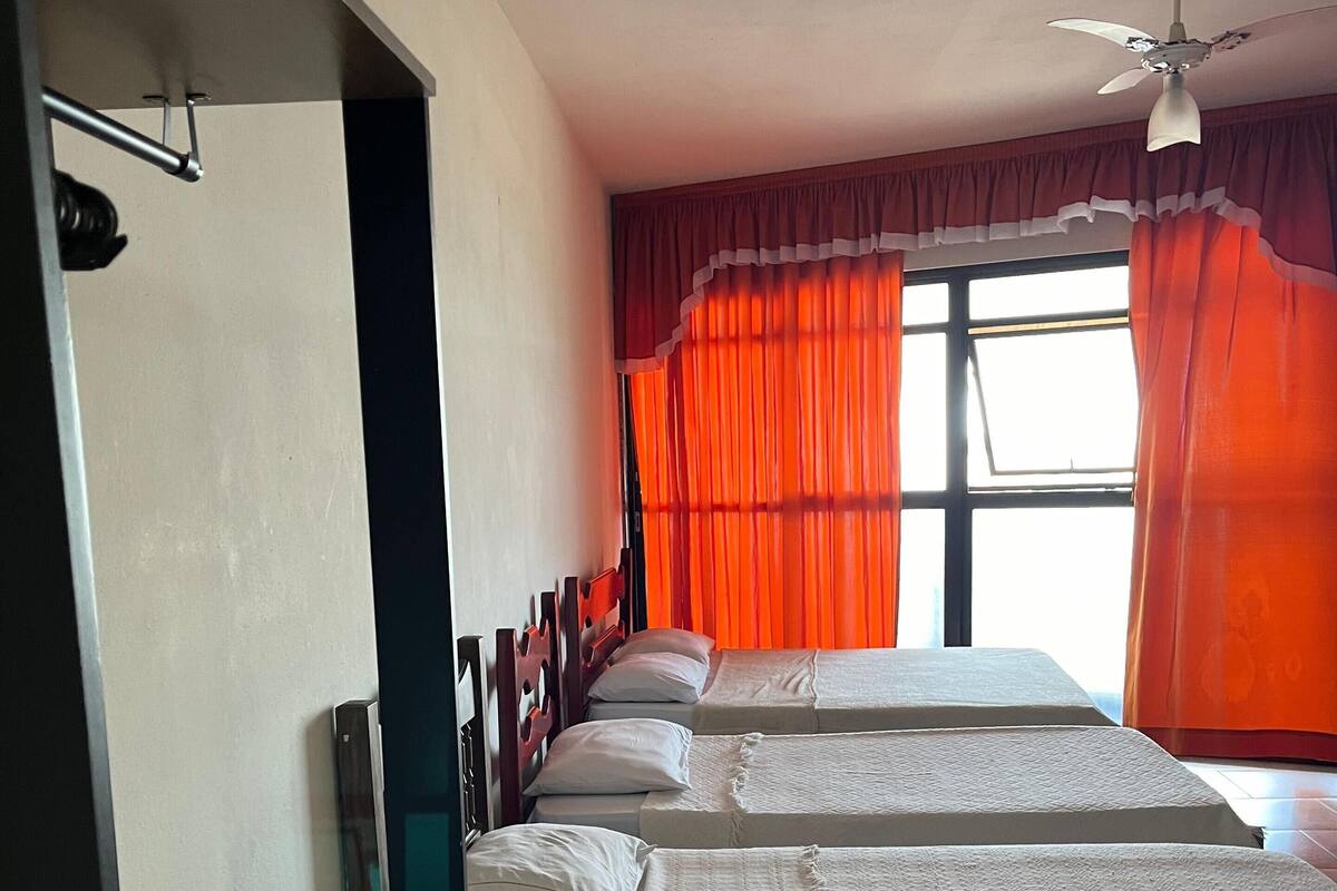 Una habitación de hotel con dos camas, un ventilador de techo y una ventana con cortinas naranjas.