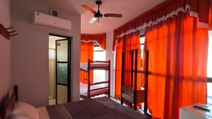 A bedroom with a bed, a ceiling fan, an air conditioning unit, a desk with a chair, and a window with orange curtains. - Hotel Art Final (Marataizes)