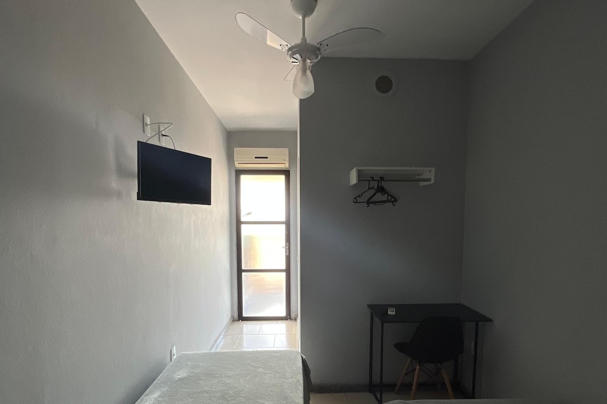 Una habitación con dos camas, ventilador de techo, televisor montado en la pared y una mesa con una silla.