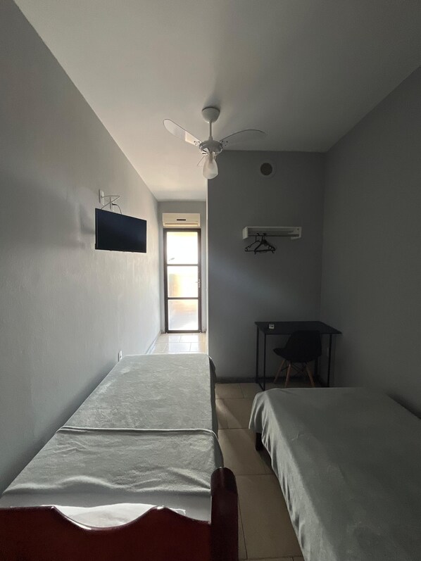 A room with two beds, a ceiling fan, a TV mounted on the wall, and a table with a chair. - Hotel Art Final (Marataizes)