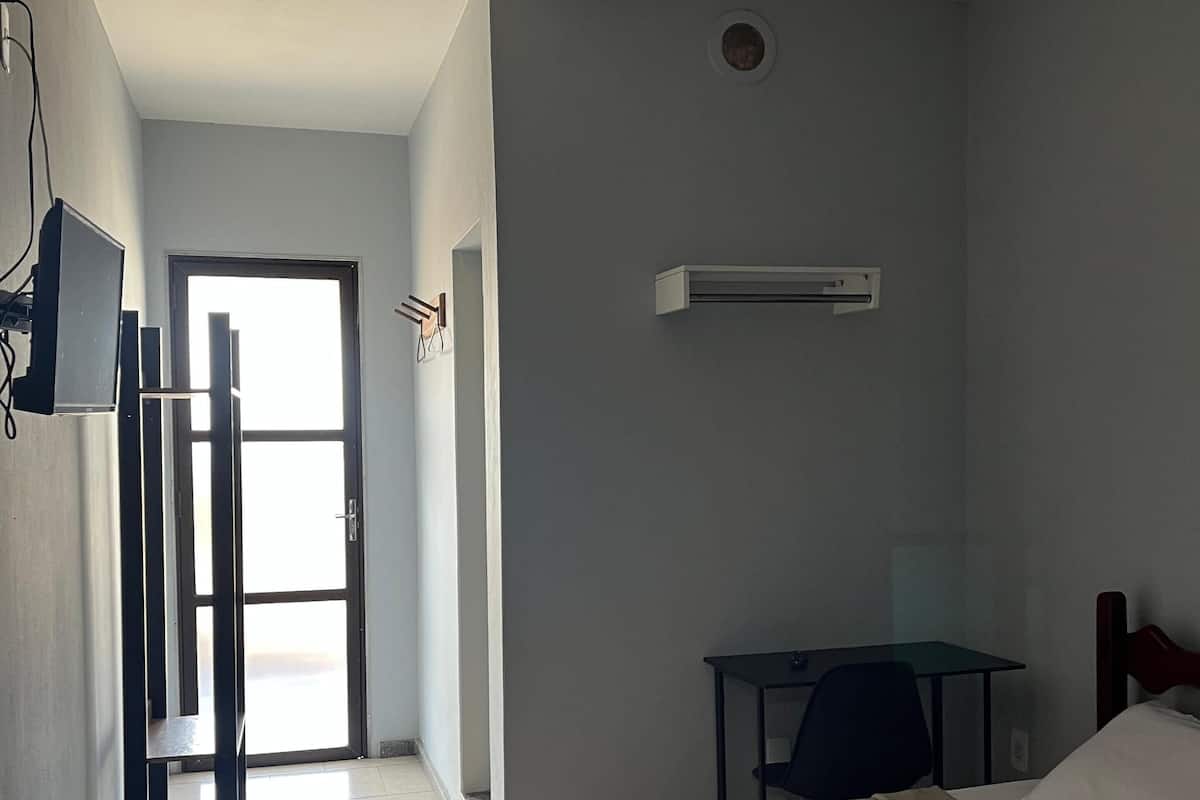 Habitación de hotel con cama, escritorio, silla, ventilador de techo y aire acondicionado.