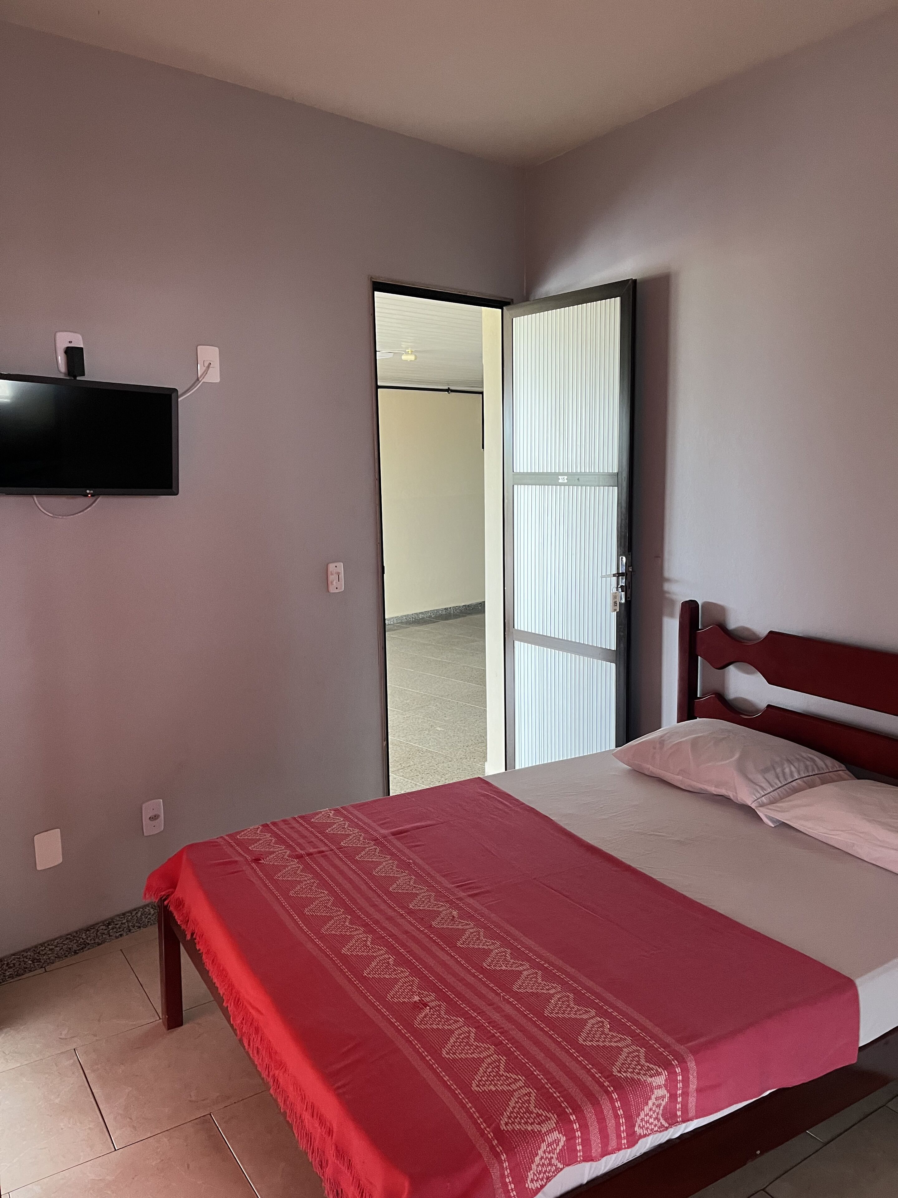 A bedroom with a bed, a TV mounted on the wall, and a door leading to a balcony.