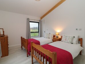 Une chambre à coucher avec deux lits en bois, une table de chevet avec une lampe, une armoire en bois et une fenêtre donnant sur un champ verdoyant.