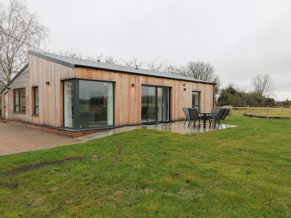Une maison moderne avec une façade en bois, de grandes portes-fenêtres coulissantes et une terrasse aménagée avec du mobilier d’extérieur.