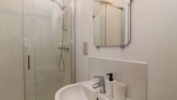 Un bagno con doccia vetrata, un lavandino con specchio sopra e un soffitto in legno.