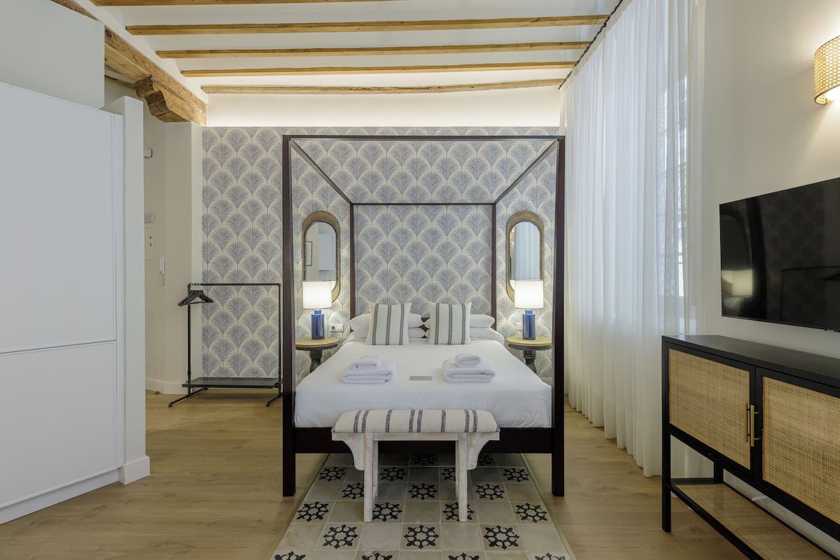 Habitación de hotel con una cama, lámparas de noche, un televisor y un papel tapiz estampado.