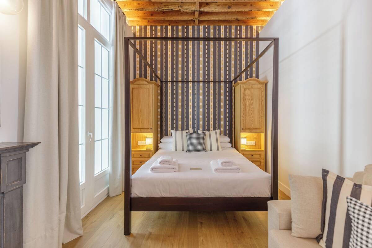 Una cama con dosel de madera, con sábanas blancas, un cabecero de madera y mesitas de noche con lámparas.
