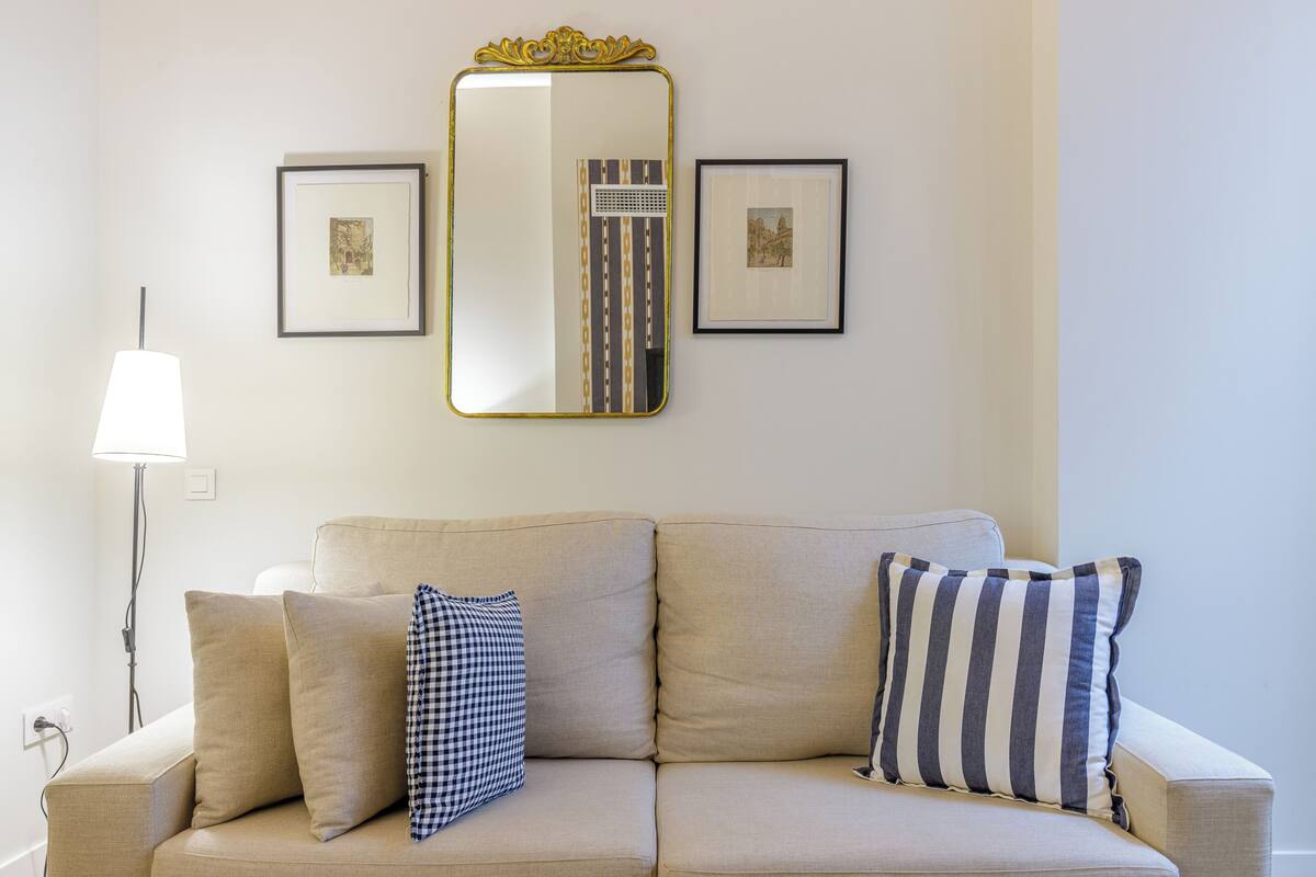 Un salón de tonos neutros con un sofá beige, dos almohadones, una lámpara de pie y tres cuadros en la pared.