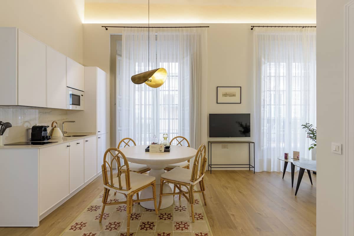 Una cocina moderna con armarios blancos, una mesa de comedor con sillas, un televisor y una pequeña mesita con una planta.
