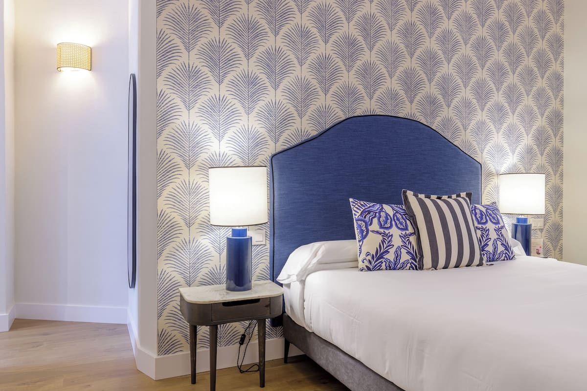 Un dormitorio ordenado con una cama grande, dos lámparas de noche y un papel tapiz estampado.