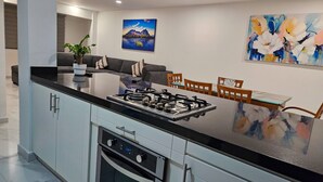 A modern kitchen with a central island, built-in oven, and dining area with wooden chairs and a glass table. - Centro Expositor, Depto 2 (Heroica Puebla de Zaragoza)