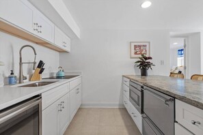 Een moderne keuken met witte kastjes, roestvrijstalen apparatuur en een granieten aanrecht.