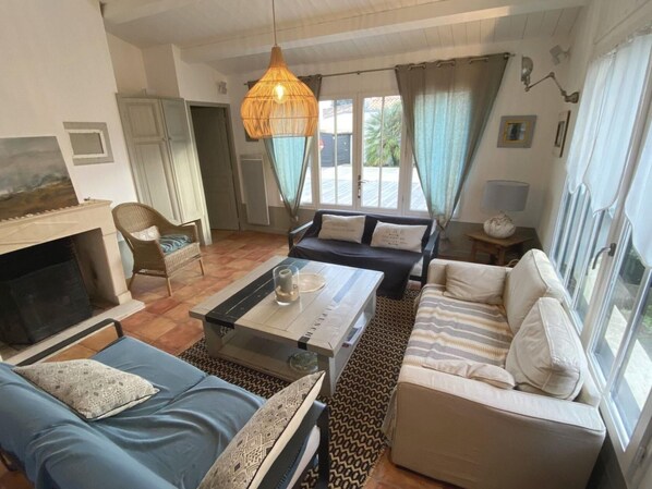 A living room with a fireplace, sofa, armchair, and a hanging light fixture.